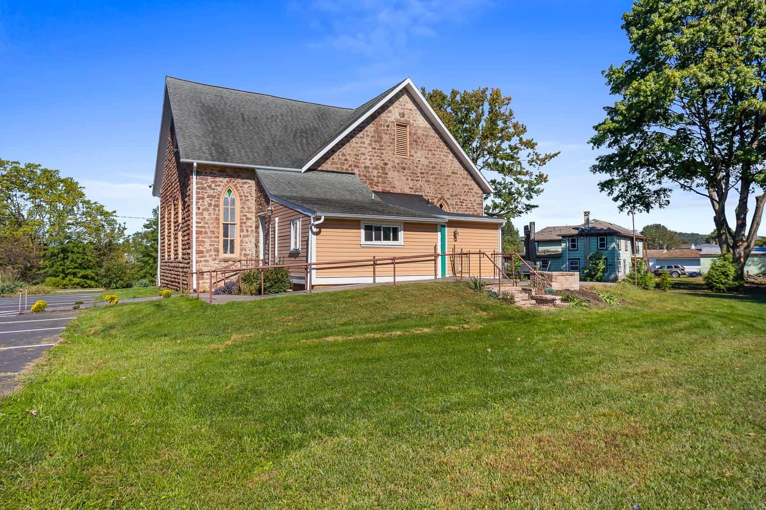 Venue-272-107 Side view of Venue 272's brick and wood chapel with a sloped roof, accessible ramp, and grassy lawn under a clear blue sky.